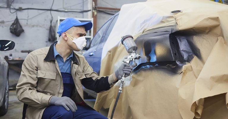 Colaborador realiza manutenção em tinta de peças de automóvel.